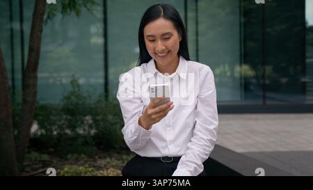 Happy Asian Korean Japanese Chinese woman record sending voice message smiling city online communicate speaker urban mobile phone smartphone girl Stock Photo
