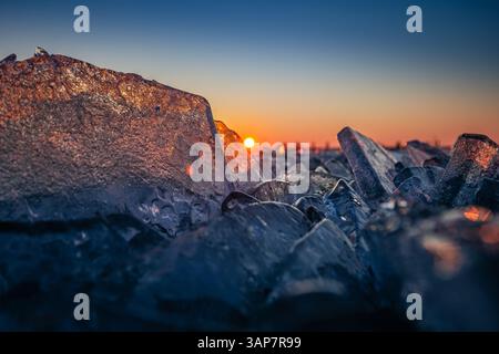 Fonyod, Hungary - Transparent ice cubes on the frozen Lake Balaton on a cold winter afternoon with golden sunset lights and clear blue sky and sun Stock Photo