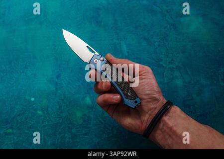 A man holds a knife in his hand. A folding knife lying in his hand. A knife on a man's palm. An outstretched hand with a knife. Stock Photo