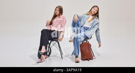 Two stylish students sitting on chairs with backpacks, relaxed and confident, ready for new school day or study session. Stock Photo