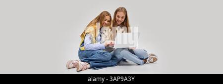 Two students sitting on floor closely collaborating with laptop, engaged in digital learning experience with curiosity and joy. Stock Photo