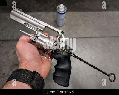 A man's hand holds a silver revolver with the cylinder open during the gun cleaning process using a cleaning rod. Stock Photo