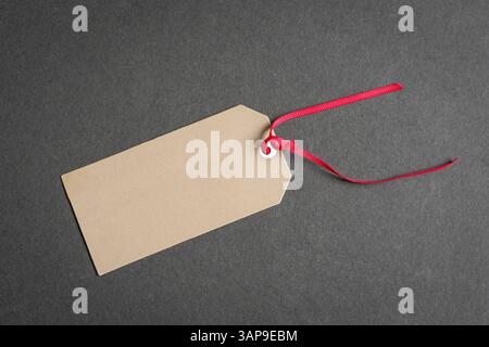 Gift tag with red ribbon on top of gray surface. Copy space. Stock Photo
