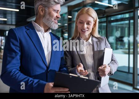 Coworkers standing together in office hall explaining business strategy using tablet Stock Photo