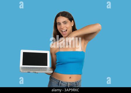 Cheerful young woman pointing at a laptop with a blank screen, suggesting online opportunities or showcasing a product Stock Photo