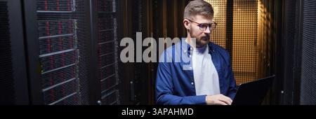 Website header shot of male IT professional working in server room with focus on network maintenance and data integrity in datacenter environment Stock Photo