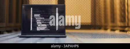 Website header shot of functional laptop displaying lines of code while situated on the floor in a data center, surrounded by rows of servers and infrastructural equipment Stock Photo