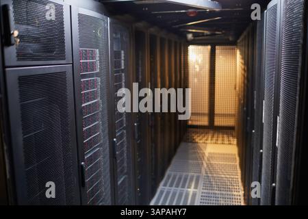 Modern server room featuring rows of black server racks and equipment creating a high-tech environment illuminated with artificial lighting Stock Photo
