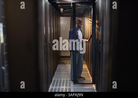 Technician performing routine maintenance in server room with various devices and gadgets around concentrating on task in data center environment Stock Photo