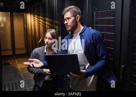 IT professionals discussing server infrastructure details in a data center environment, featuring extensive server racks and high-tech hardware. Collaborative work in a technology-driven setting Stock Photo