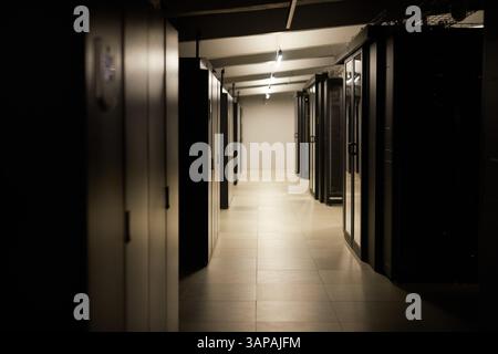 Long hallway in data center, featuring aligned server racks on both sides. Overhead lighting casts a warm glow creating an organized and efficient atmosphere Stock Photo