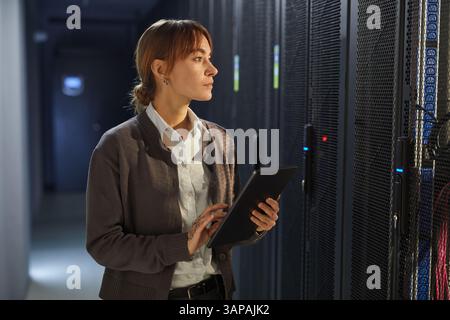 Asian woman with tablet checking server racks in data center illuminating from server lights. Modern technology environment with significant attention to equipment and cooling systems Stock Photo