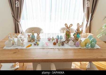 Easter decorations fill a wooden table, featuring bunny figurines and colorful eggs. The arrangement includes ceramic bunnies, plush bunnies, and Stock Photo
