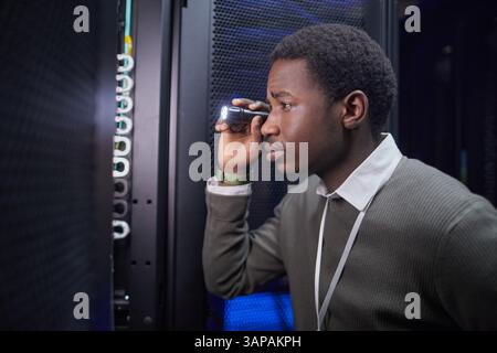 Focused IT technician inspecting server racks with flashlight while ensuring performance and security in modern data center environment Stock Photo