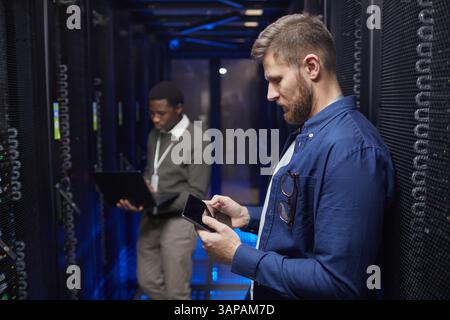 Engineers working in a modern data center server room, checking devices and maintaining server racks, ensuring optimal performance. Technicians collaborating in a professional and secure environment Stock Photo
