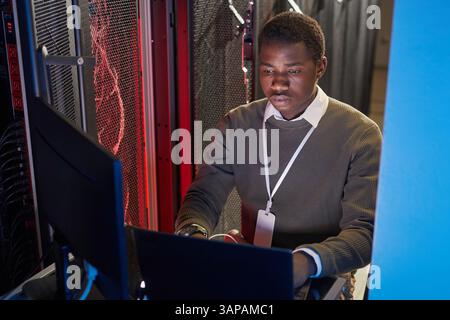 Portrait of dedicated IT technician concentrating on his tasks in server room, surrounded by technology and servers, demonstrating commitment to his profession Stock Photo