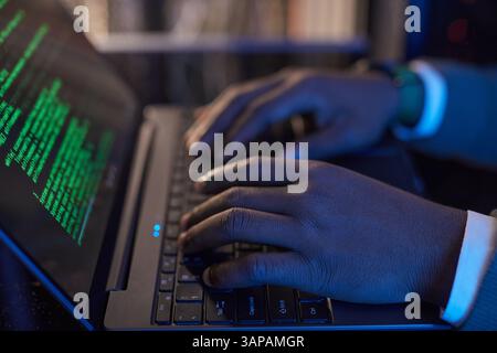 Hands typing code on laptop with green text on screen, wearing a wristwatch, creating programming environment on dark workspace without using natural light Stock Photo