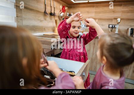 Three children gather around a kitchen drawer, filled with various utensils. One child excitedly holds up a measuring cup, sharing the fun of discover Stock Photo