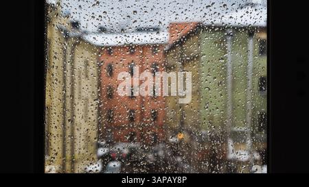 Raindrops sliding on window glass blurring buildings in the background Stock Photo