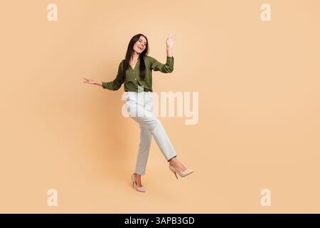 Smiling young woman in formal attire posing joyfully with dynamic gestures against a warm beige background Stock Photo