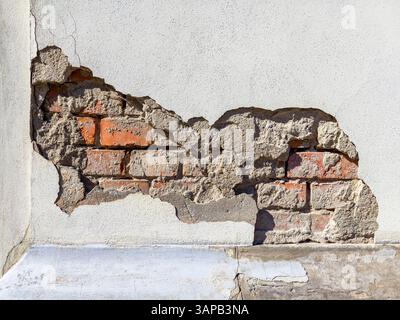 Close-up of a section of weathered plaster wall showing a gap where the plaster has cracked and peeled away, revealing the underlying brickwork. Stock Photo