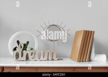 Small mirror, books and florarium on white table near grey wall, closeup Stock Photo