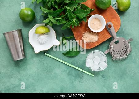 Wooden cutting board, shaker, strainer and ingredients for mojito on green background Stock Photo