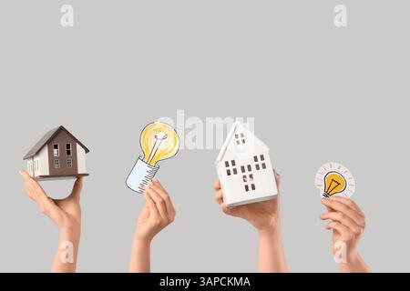 Female hands with house models and paper light bulbs on light background. Ecology concept Stock Photo