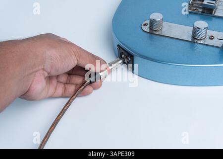Close-up of a hand plugging an audio cable into the body of a blue electric guitar. Isolated on a white background. Stock Photo