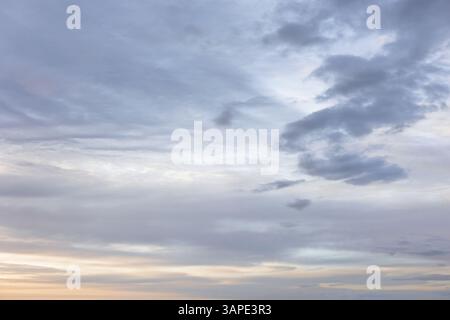 Moody Layers of Grey Clouds in Sky at Dusk with Soft Warm Orange Light Breaking near Horizon Stock Photo
