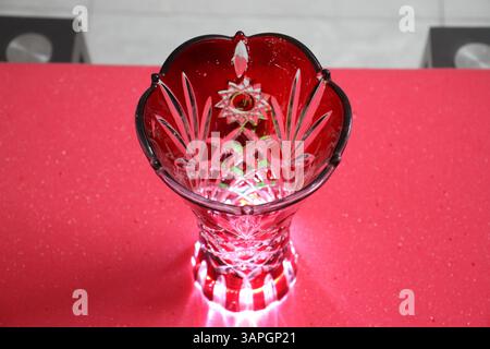 A glass made red colored flower vase with bright light stands on table. Stock Photo