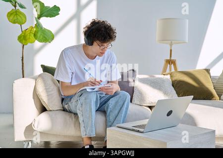 Young student guy in headphones sitting at home on with laptop taking notes Stock Photo