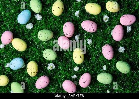 Vibrant, speckled Easter eggs in pastel colors are scattered across green grass, surrounded by delicate white flowers, symbolizing spring joy. Stock Photo