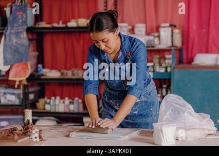 Mexican woman, 24, prepares clay in her artisan workshop before molding. Scene captures the beginning of the ceramic-making process and focus Stock Photo