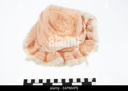 This peach knit wool bonnet with white trim is a doll accessory from the Missouri Historical Society collection, demonstrating 19th-century craftsmanship in miniature textile design. Stock Photo