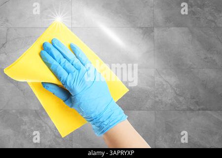 Cleaning service worker in rubber glove washing grey tiled wall with rag, closeup. Shine of purity on cloth Stock Photo