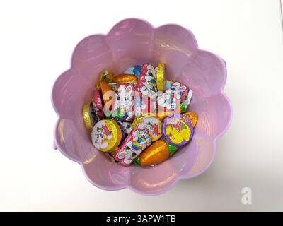 Colorful Easter chocolates in a shiny purple flower-shaped bowl on a white background. Festive candy assortment perfect spring celebrations, holiday Stock Photo