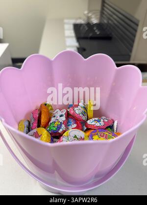 Colorful Easter chocolates in a shiny purple flower-shaped bowl on a white background. Festive candy assortment perfect spring celebrations, holiday Stock Photo