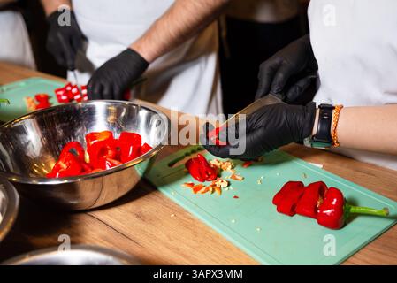 Close-up of chefs cutting red bell peppers on green cutting boards, preparing ingredients in a professional kitchen setting. Stock Photo