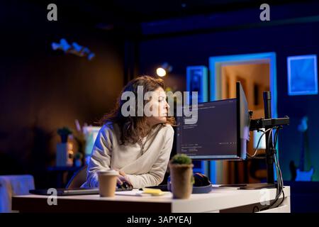 System administrator doing software debugging on PC at home, checking broken lines of code displayed on monitors. Proficient IT specialist in apartment fixing coding problems, typing on keyboard Stock Photo