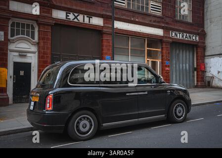 Black London Taxi Parked on a Quiet Street with Red Brick Building Stock Photo