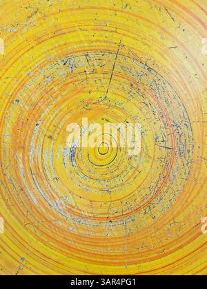 A close-up shot of a round tabletop in a garden, featuring an abstract circular pattern created with yellow and orange paint. The paint is cracked and Stock Photo