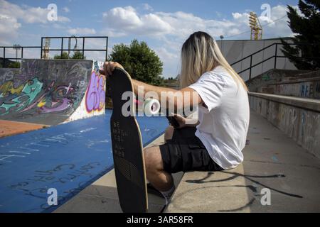 Portrait of guy with long hair using cell phone with his skateboard in the street Stock Photo