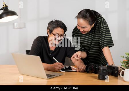 Asian young friendly pretty success female photographer sit smile hold and point dslr camera screen in hands try to check choose best. Photographer an Stock Photo