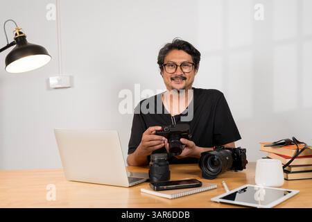Portrait of a thoughtful bearded photographer sitting staring at the camera, computer screen at the desk, working concept. Stock Photo