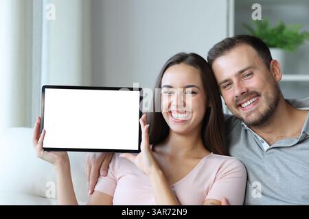 Happy couple showing blank digital tablet screen sitting on a couch at home Stock Photo