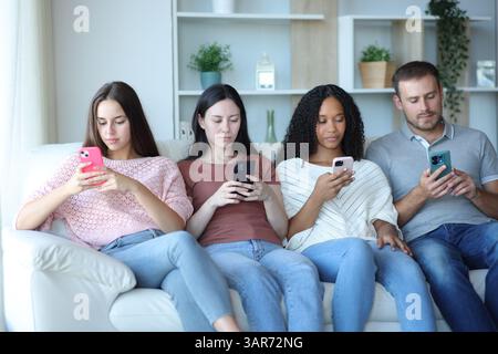 Interracial group of friends using everyone their phones sitting on a couch at home Stock Photo