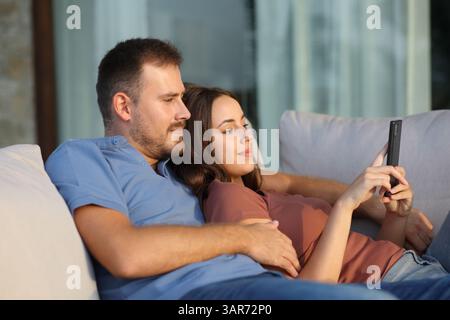 Relaxed couple checking smart phone sitting on a sofa in a terrace Stock Photo