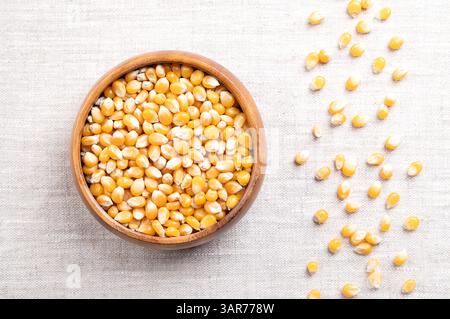 Unpopped popcorn kernels in a wooden bowl on linen. Seeds of Zea mays variety everta, rounded at the top, which expand and puffs up, when heated. Stock Photo
