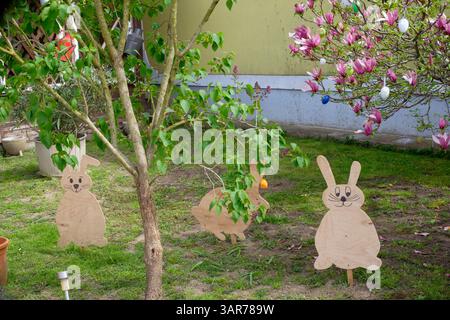 rural village house garden with small colourful easter eggs hanging from tree alongside homemade wooden bunny rabbits lentikapolna zala county hungary Stock Photo